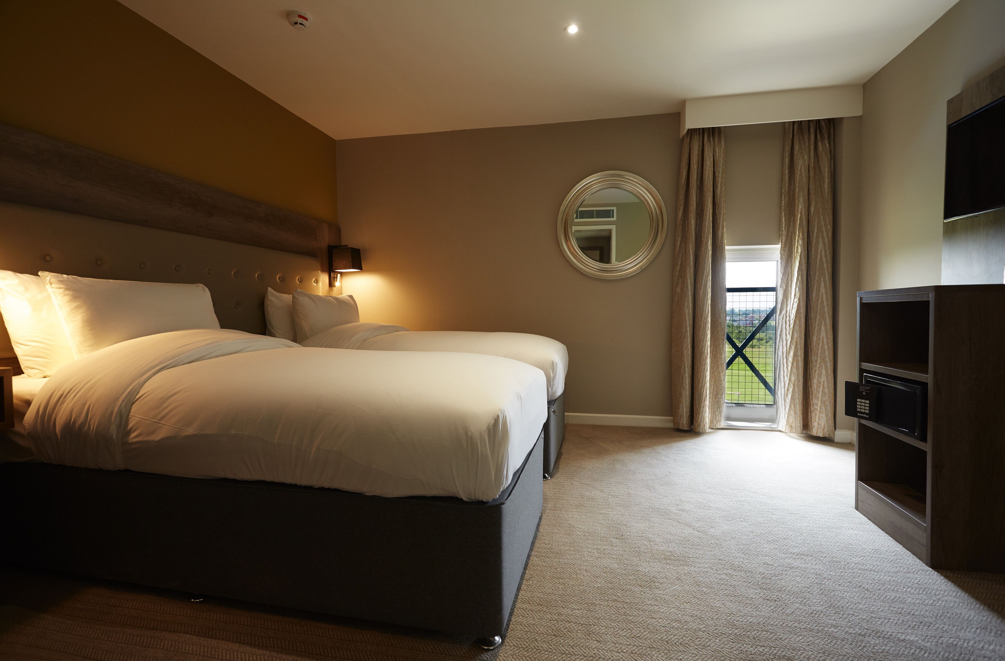 Une chambre d’hôtel avec deux lits, un grand miroir, une télévision et une vue sur l’extérieur.