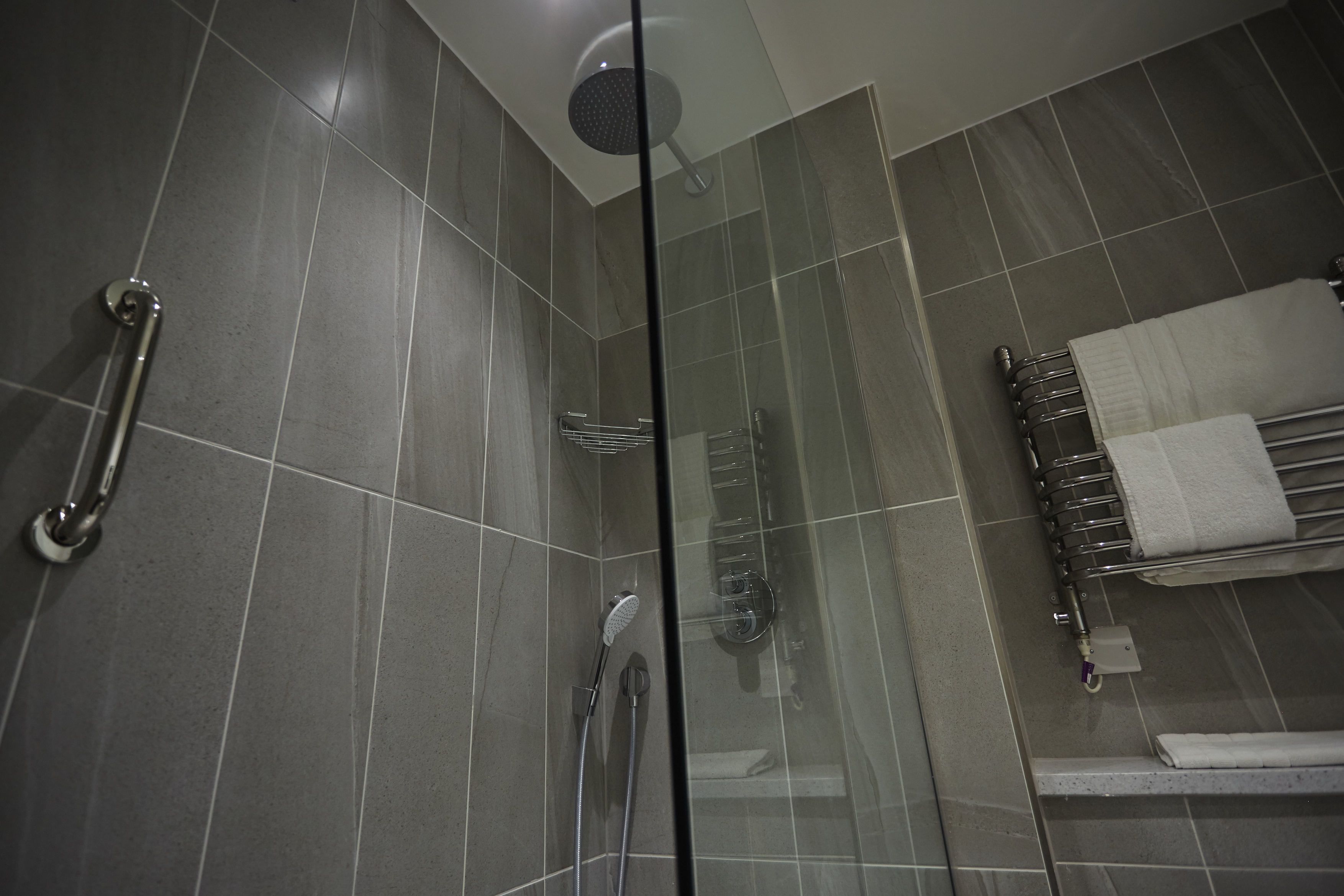 A modern shower area with a glass partition, a handrail, and a towel rack.