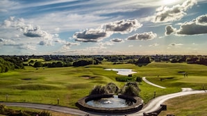 A golf course with a circular pond, a road, and a distant town. - Wychwood Park (Crewe)