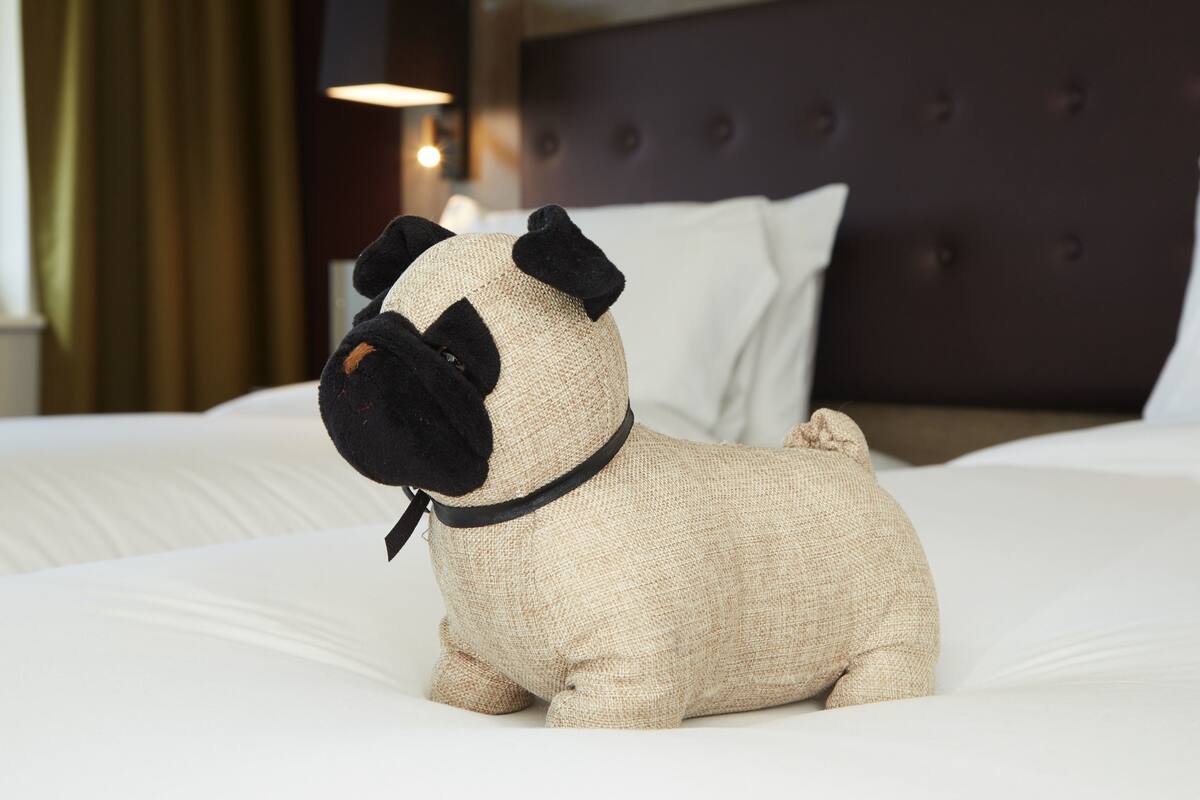 A plush dog toy on a bed with a tufted headboard and white pillows.