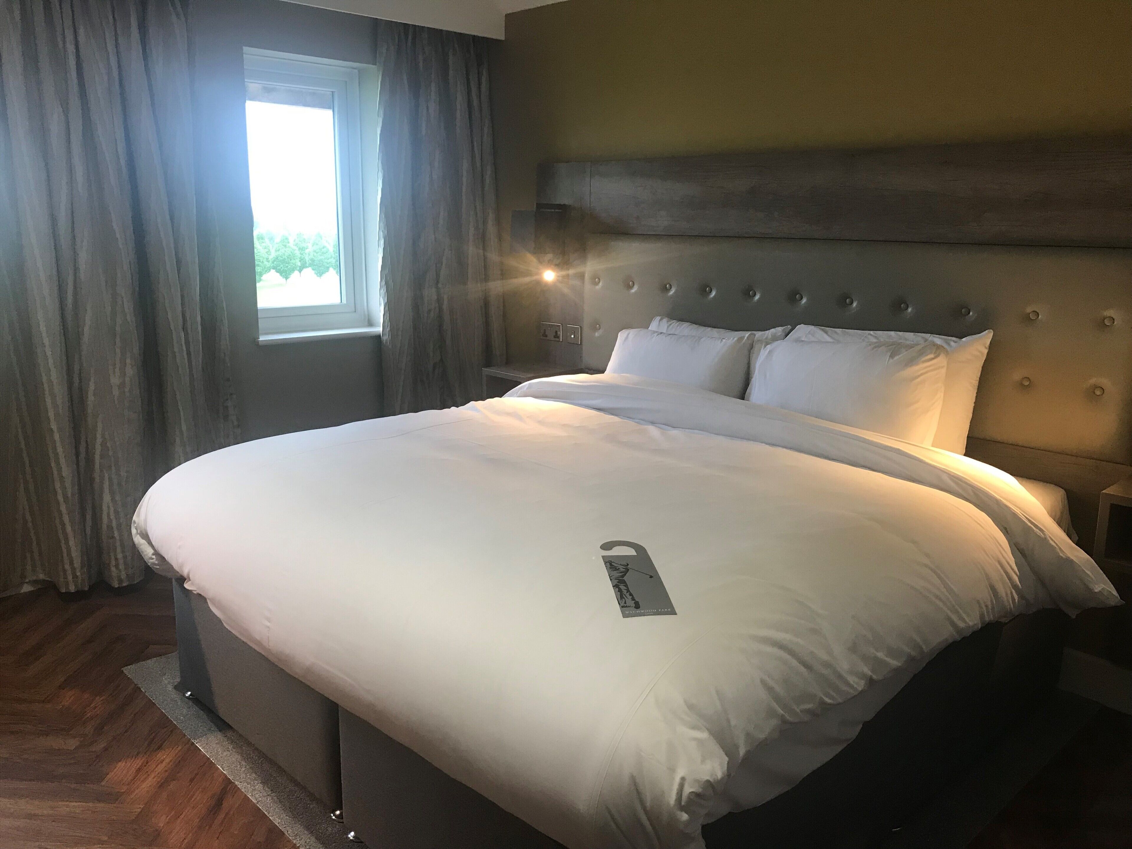 A neatly made bed with white linens, a headboard with circular details, and a window with curtains.