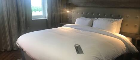 A neatly made bed with white linens, a headboard with circular details, and a window with curtains.