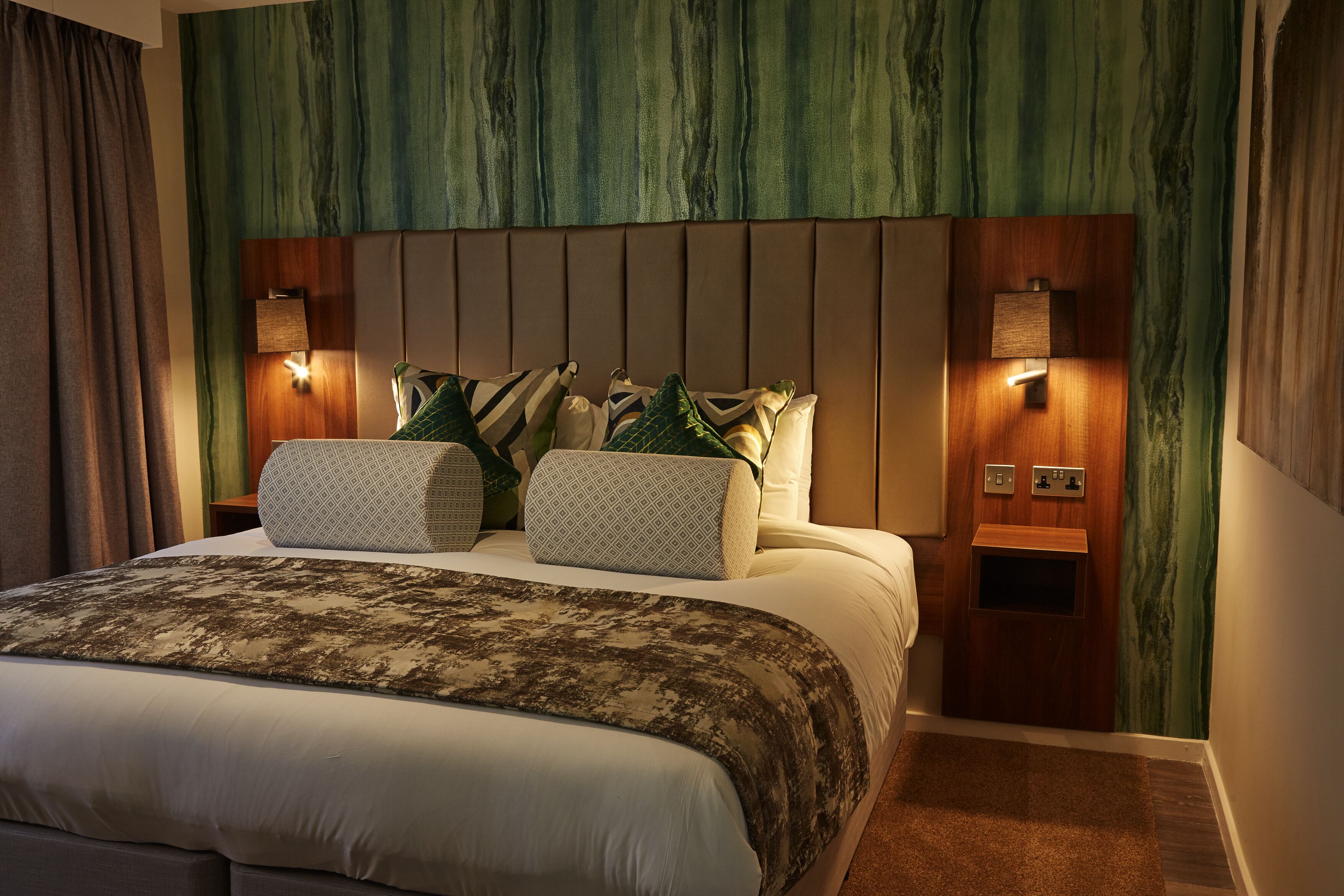 Un dormitorio con una cama grande, dos mesitas de noche con lámparas, un cabecero con diseño de paneles de madera y una pared verde con textura.