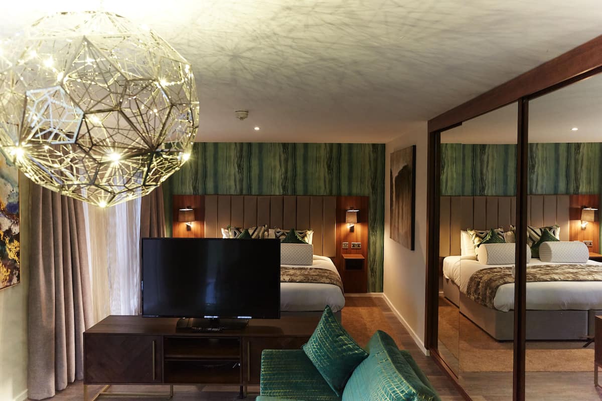 A modern hotel room with a large TV, a green sofa, and a unique spherical light fixture.