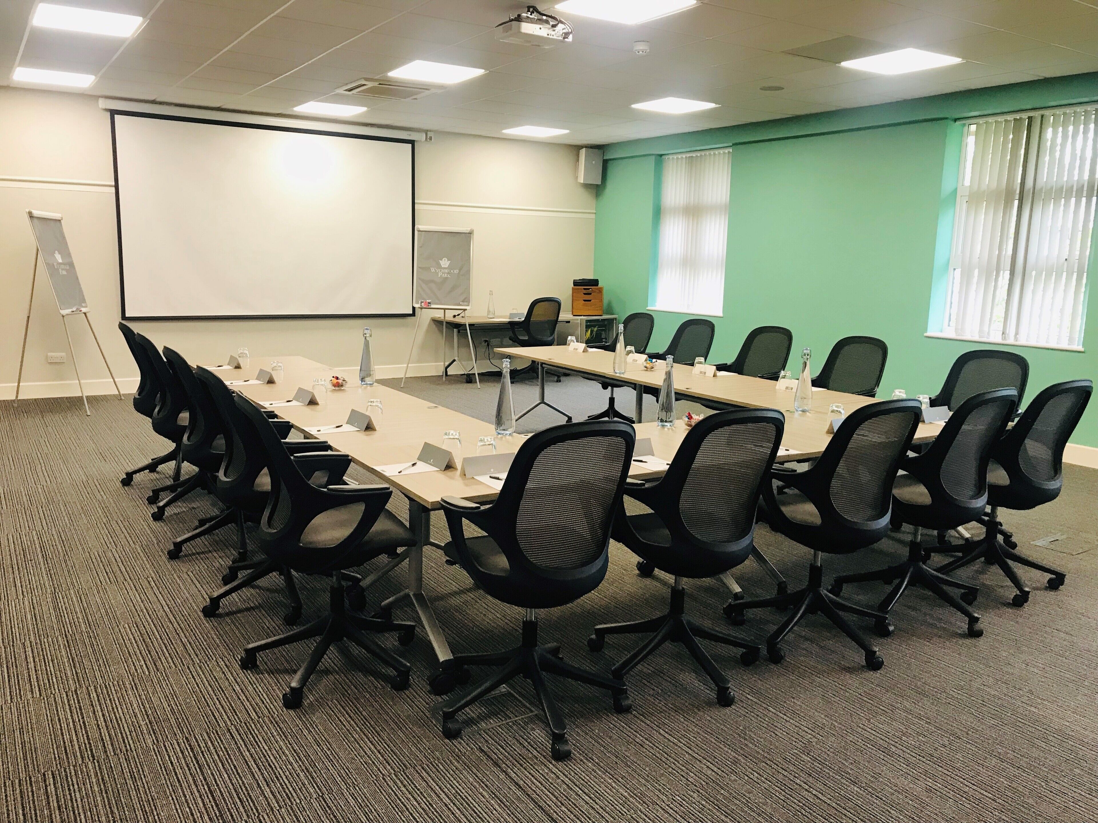 A conference room with a long table, chairs, a projector screen, and a whiteboard.