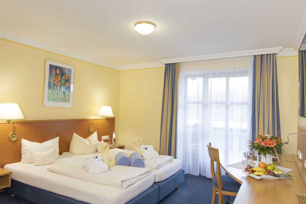 Une chambre d’hôtel avec deux lits, un bureau agrémenté d’un vase de fleurs et un tableau au mur.