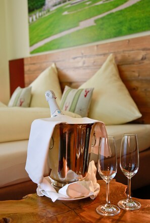 A champagne bottle on a table with two glasses, a wooden table, and a sofa with pillows in a room with a painting on the wall. - Hotel Schmelmer Hof (Bad Aibling)