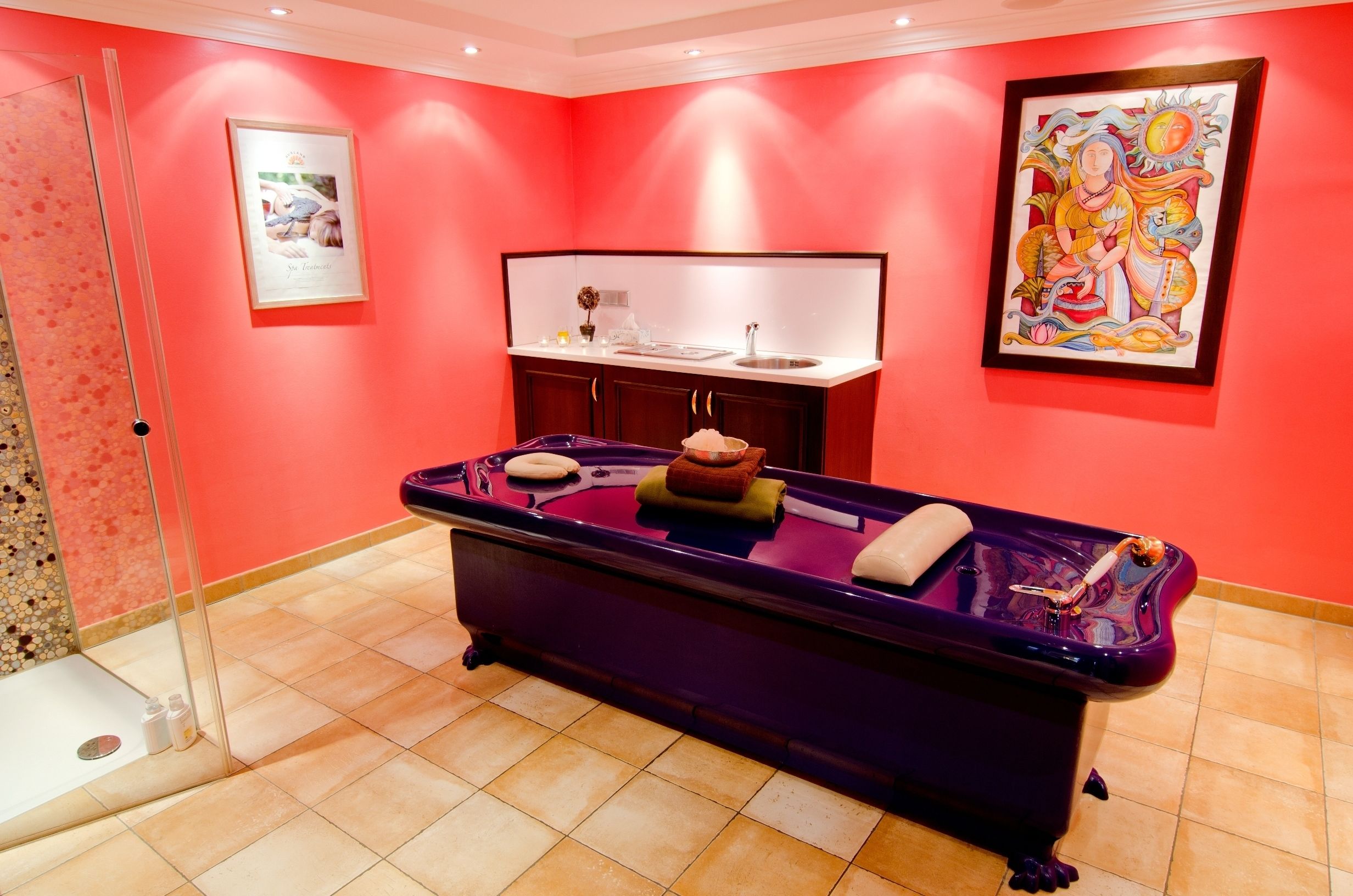 A room with a purple massage table, a sink, and a framed painting on the wall.