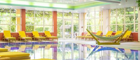 An indoor swimming pool with yellow lounge chairs and a hammock.
