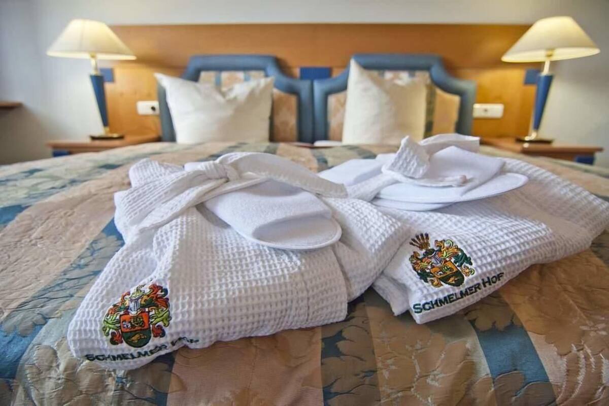 Un lit avec deux serviettes blanches ornées d’un blason, une tête de lit en bois et des lampes de chevet.