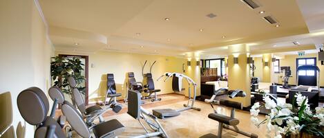A well-lit gym with various exercise equipment, a reception area, and a seating area with a plant.