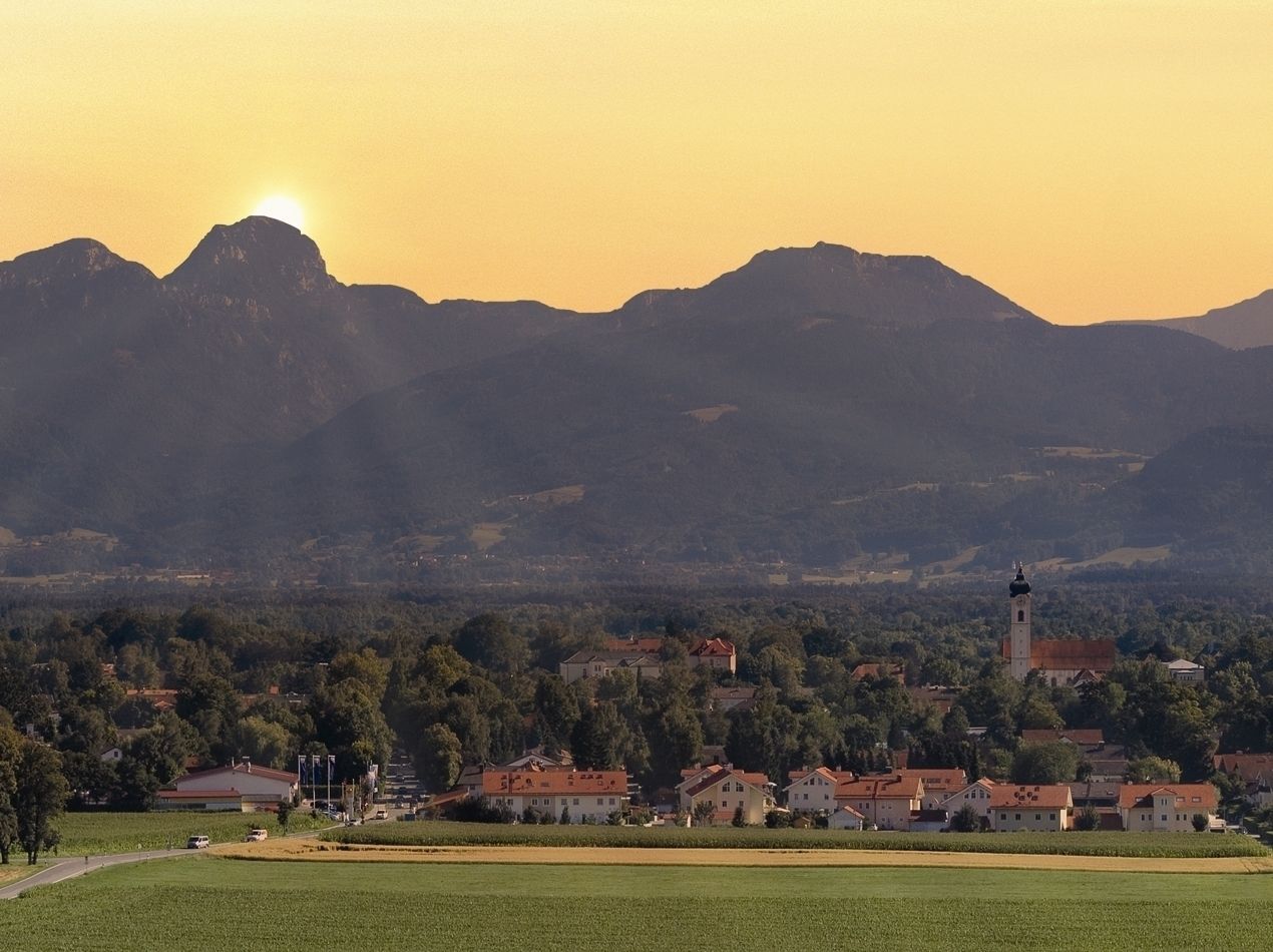 A rural landscape with a church, houses, and mountains in the background.