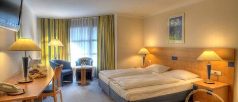 A hotel room with a bed, two bedside tables with lamps, a desk with a chair, a small table with a vase, and a television mounted on the wall.