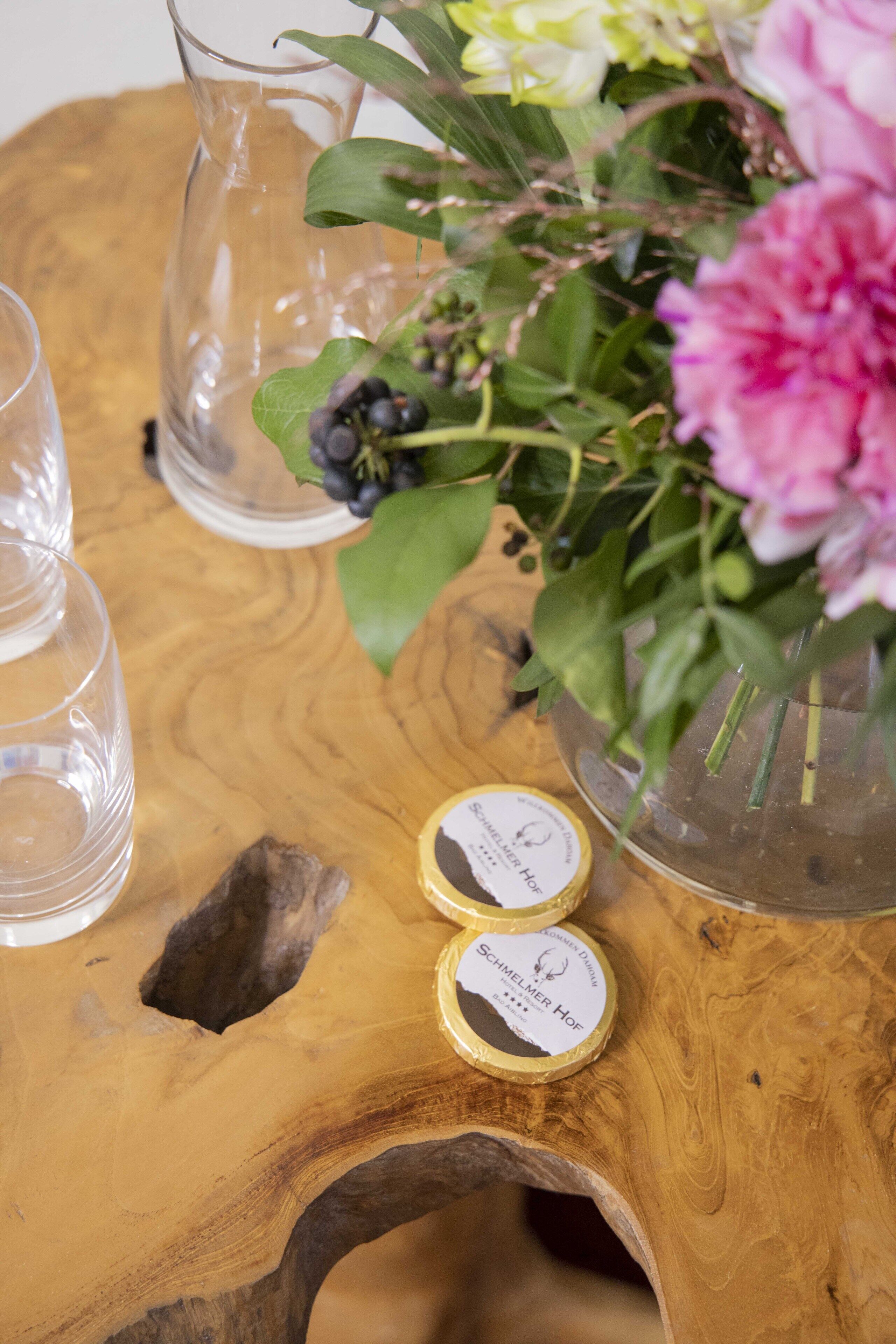 Ein Holztisch mit einer Glaskaraffe, Blumen und zwei kleinen Behältern.