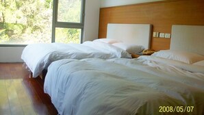 A hotel room with two beds, a wooden headboard, a nightstand, and a window with a view of trees. - Tsauing Spa Vacation Hotel (Gukeng)