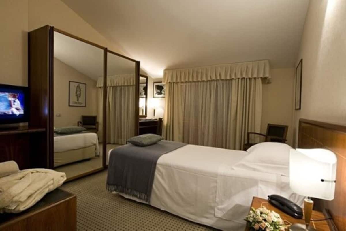 A hotel room with a bed, a television, a desk with a lamp, and a mirror.