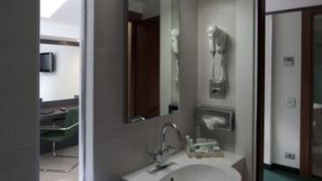 Un baño moderno con un ventanal grande, un lavamanos blanco, un espejo y un secador de pelo montado en la pared.