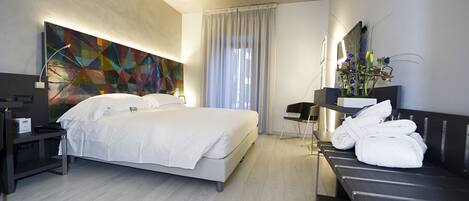 A modern hotel room with a large bed, a desk with a chair, a vanity with a mirror, and a bathroom with a shower.