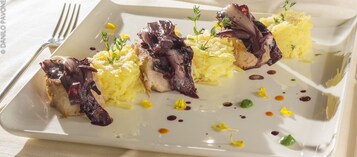 Un piatto bianco rettangolare con un'ordinata porzione di purè di patate guarnito con fette di carne ed erbe aromatiche.