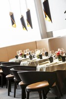 Un'area pranzo con tavoli apparecchiati, sedie e lampade a sospensione.