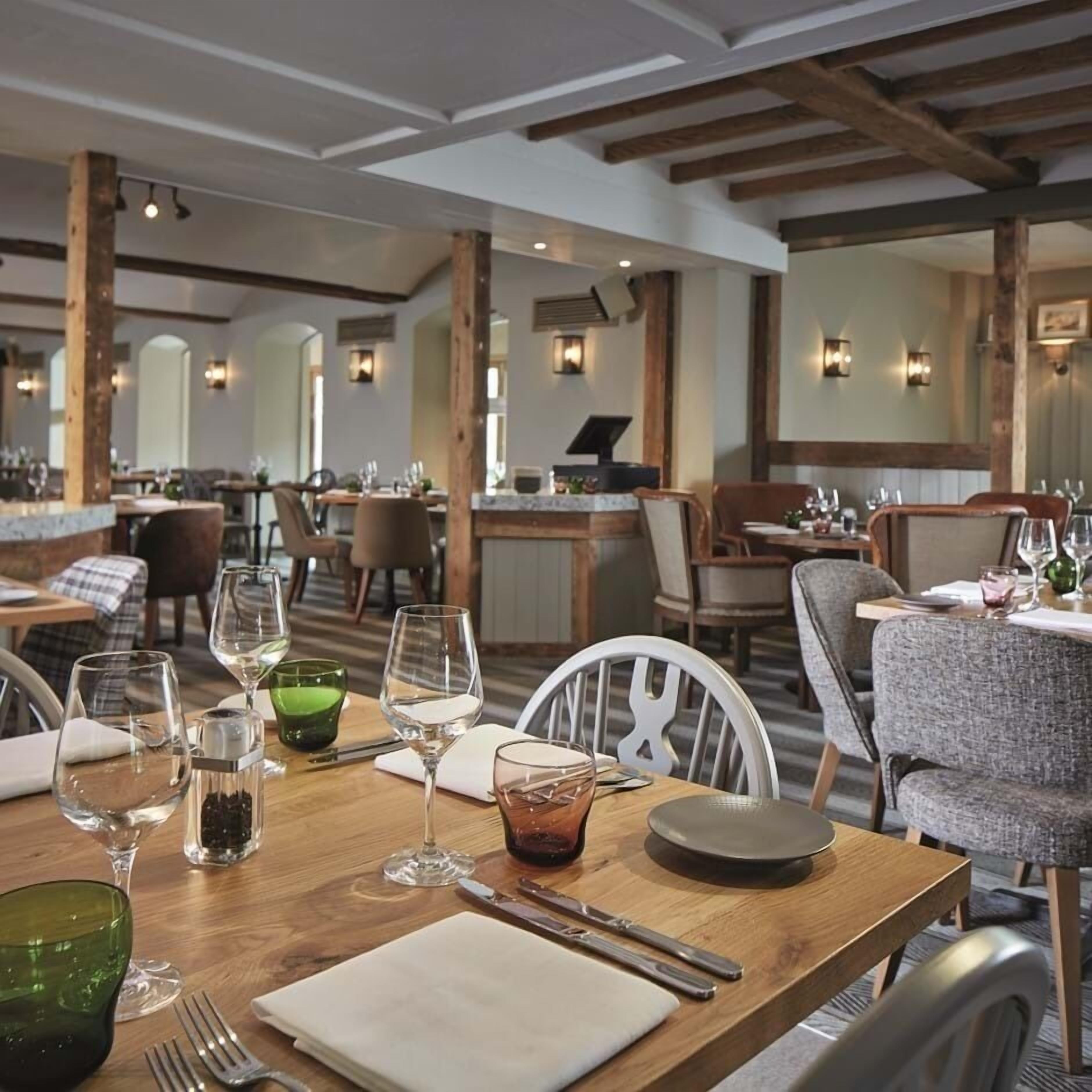 A restaurant interior with wooden tables, chairs, and a bar area.