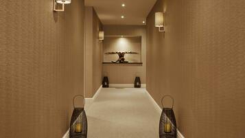 A hallway with textured walls, recessed ceiling lights, a central art piece, and two wall-mounted lanterns.