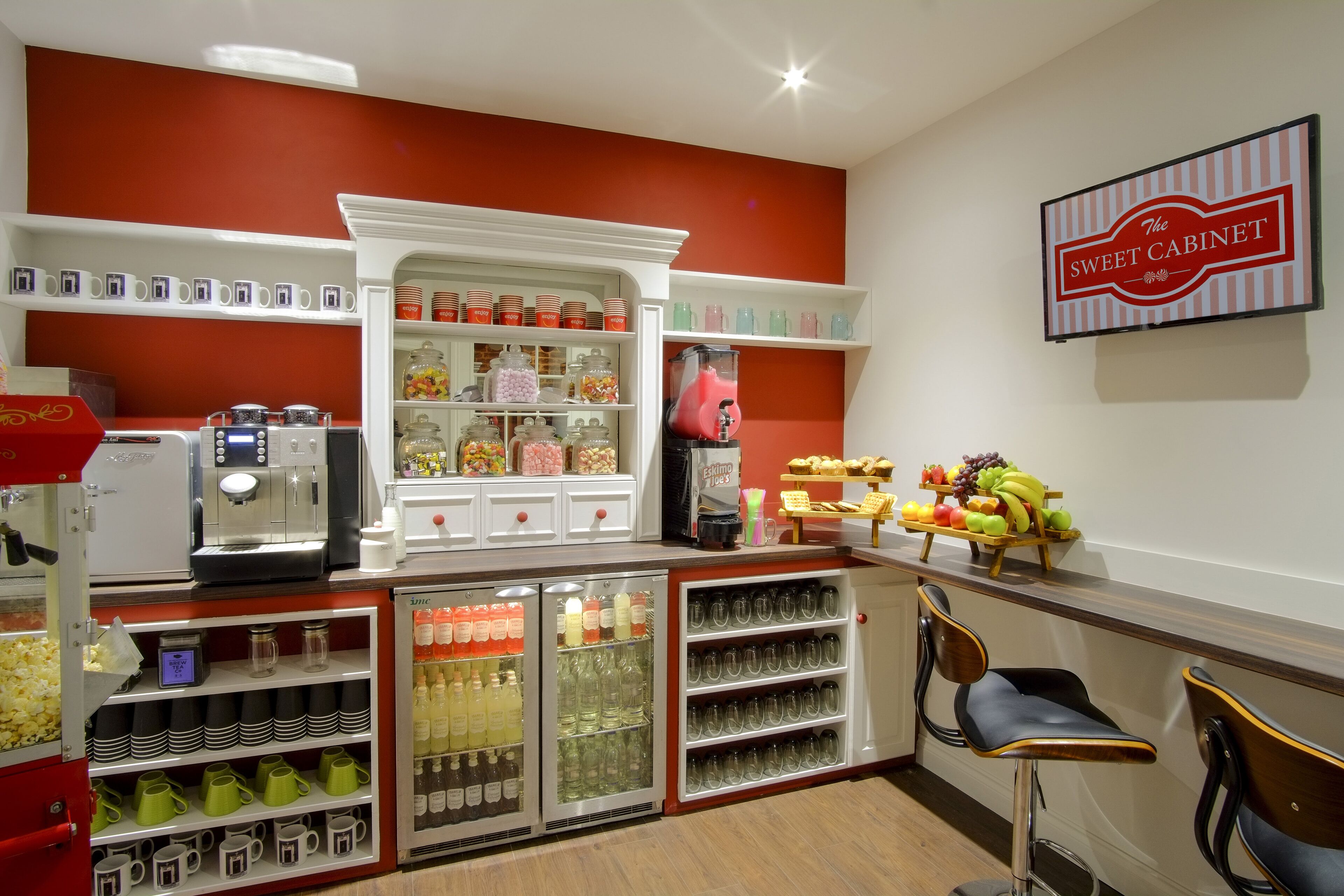 A kitchen area with a coffee machine, shelves with jars, and a sign reading "The Sweet Cabinet".