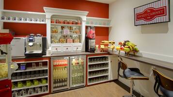 A kitchen area with a coffee machine, shelves with jars, and a sign reading "The Sweet Cabinet".