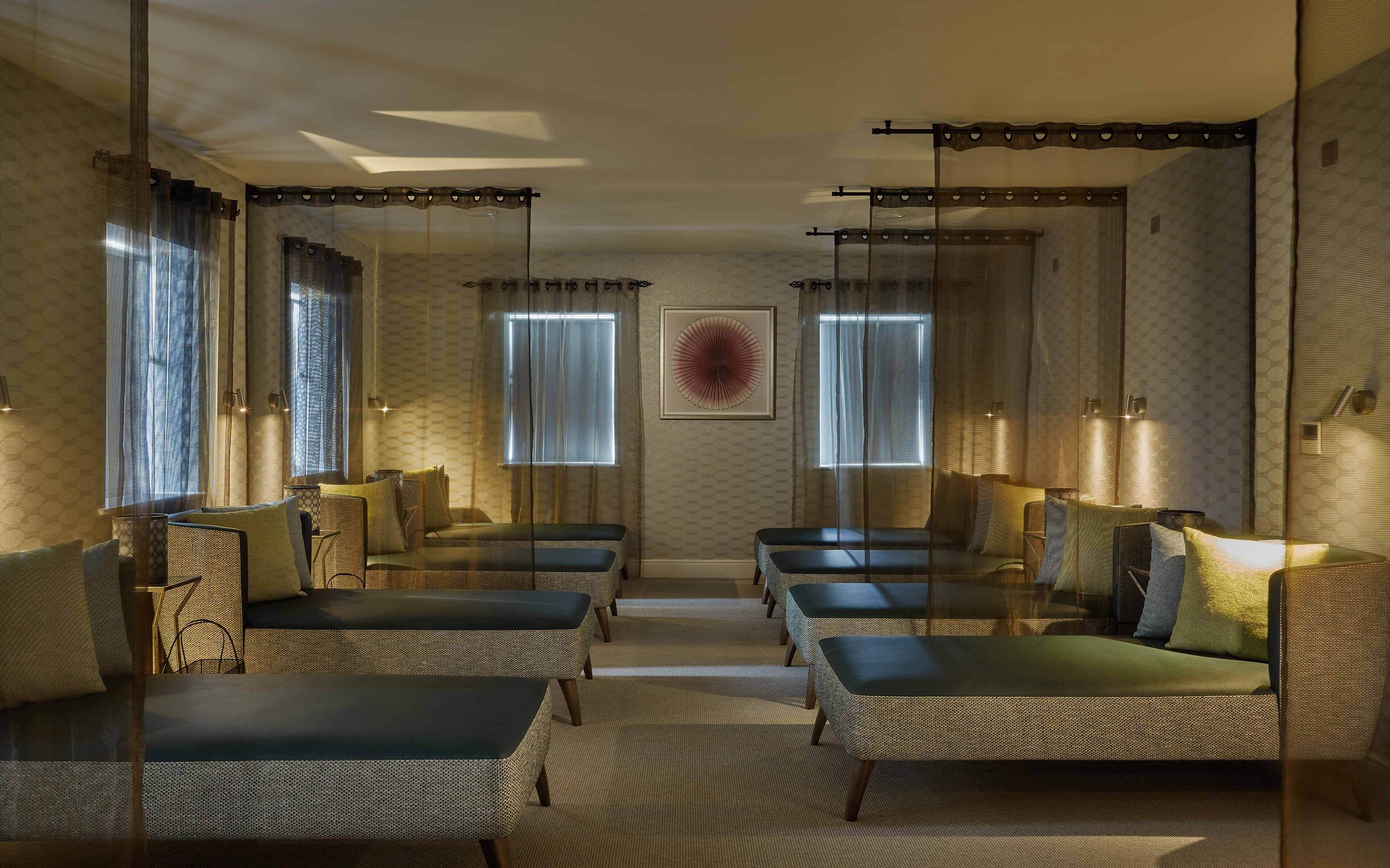 A hotel room with a central seating area, large windows with curtains, and a framed artwork on the wall.