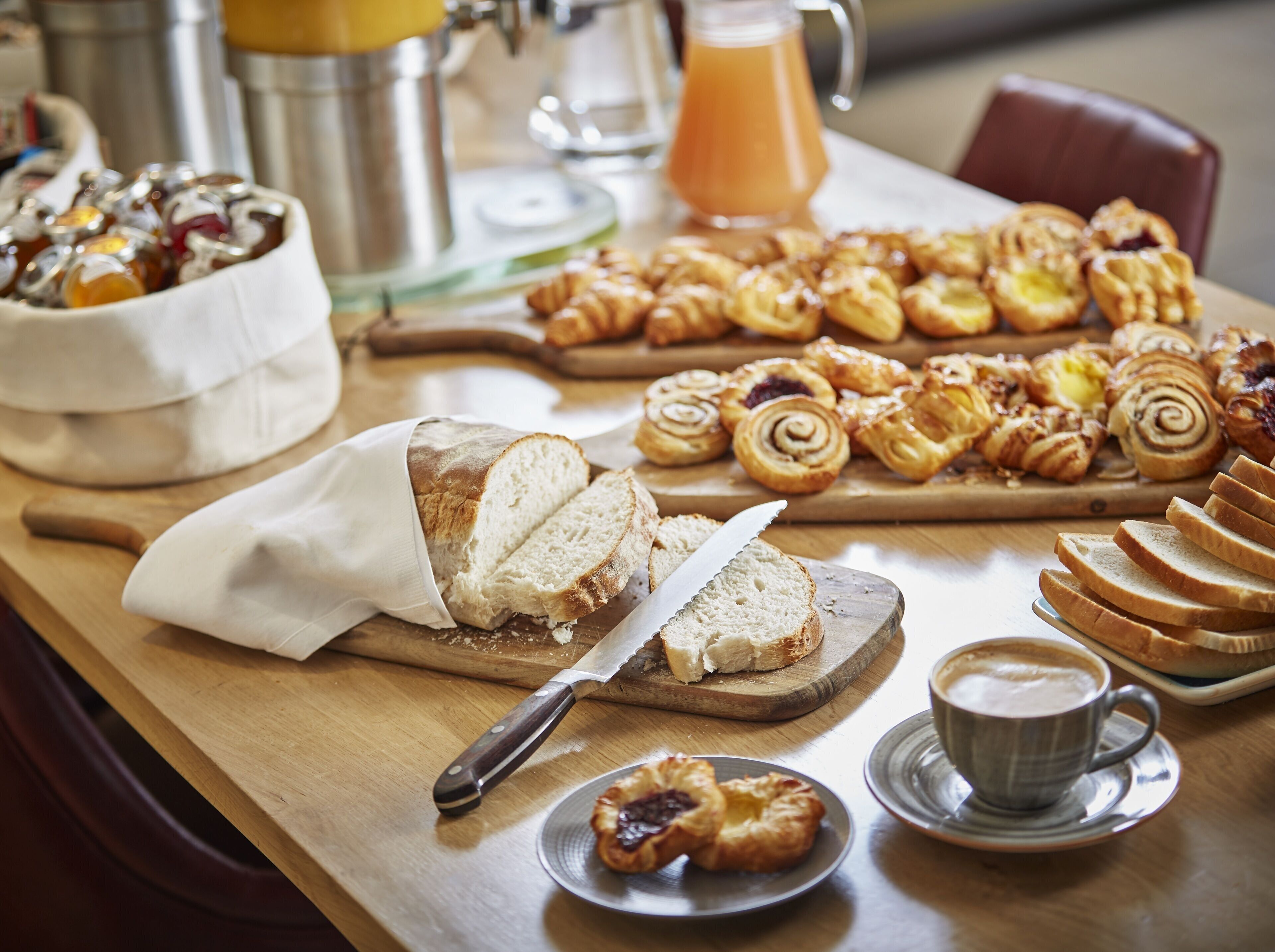 Un bufé de desayuno con diversos pasteles, pan y una taza de café sobre una mesa de madera.