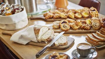 Un bufé de desayuno con diversos pasteles, pan y una taza de café sobre una mesa de madera.