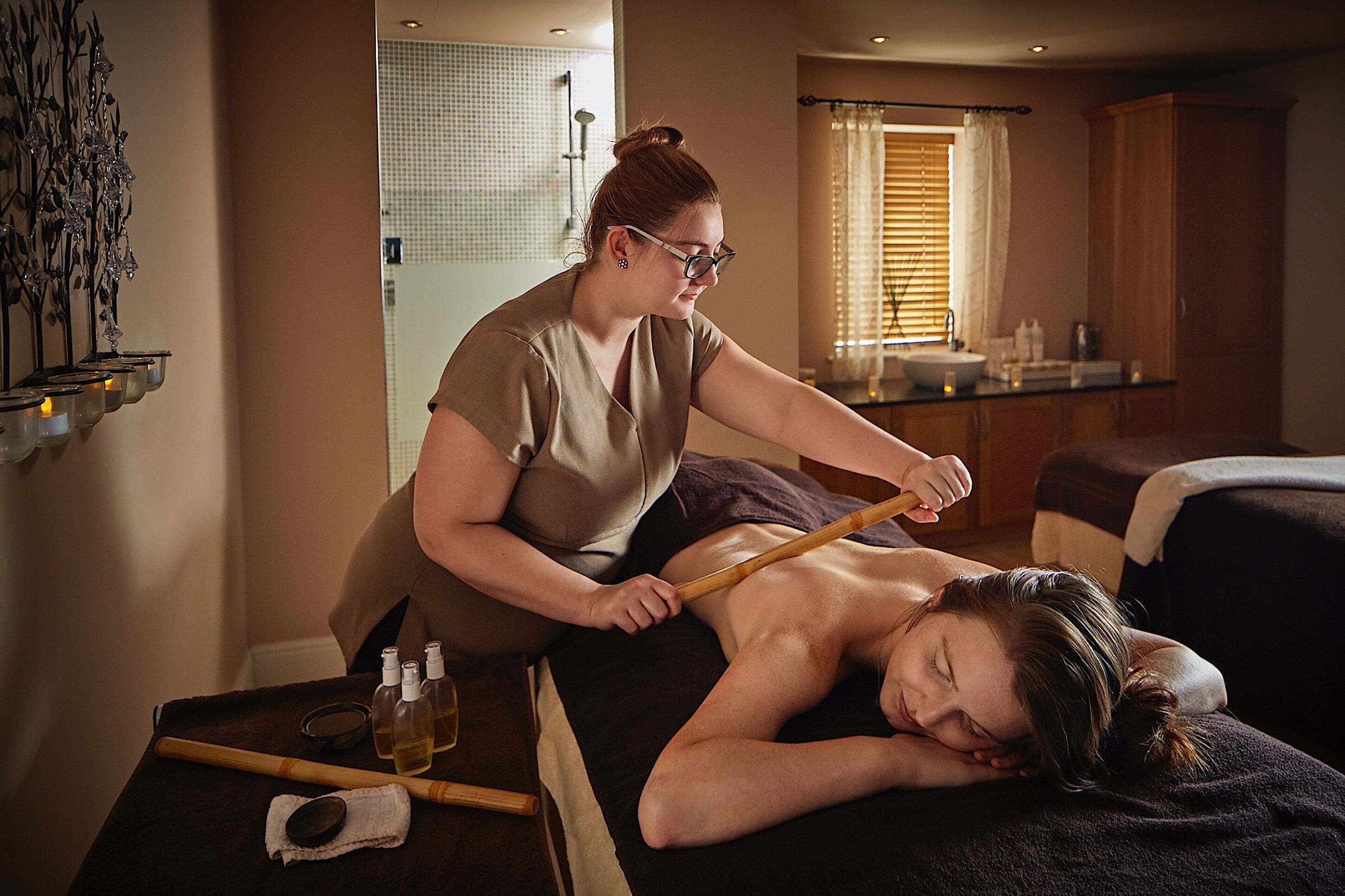 A massage therapy session in a room with a wooden cabinet, a sink, and a window with blinds.