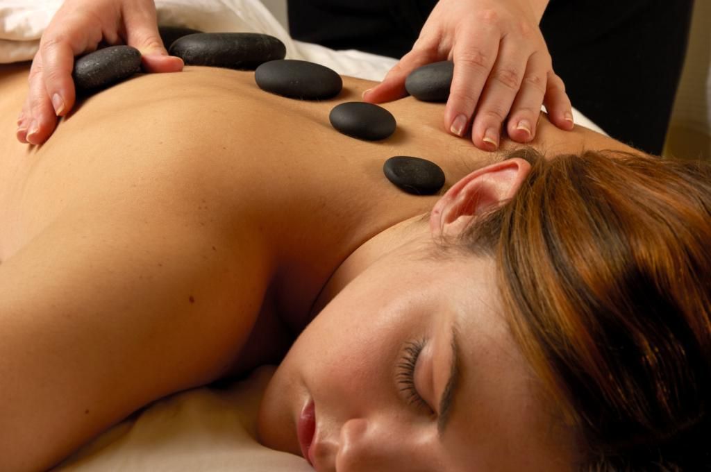 A person receiving a back massage with black stones.