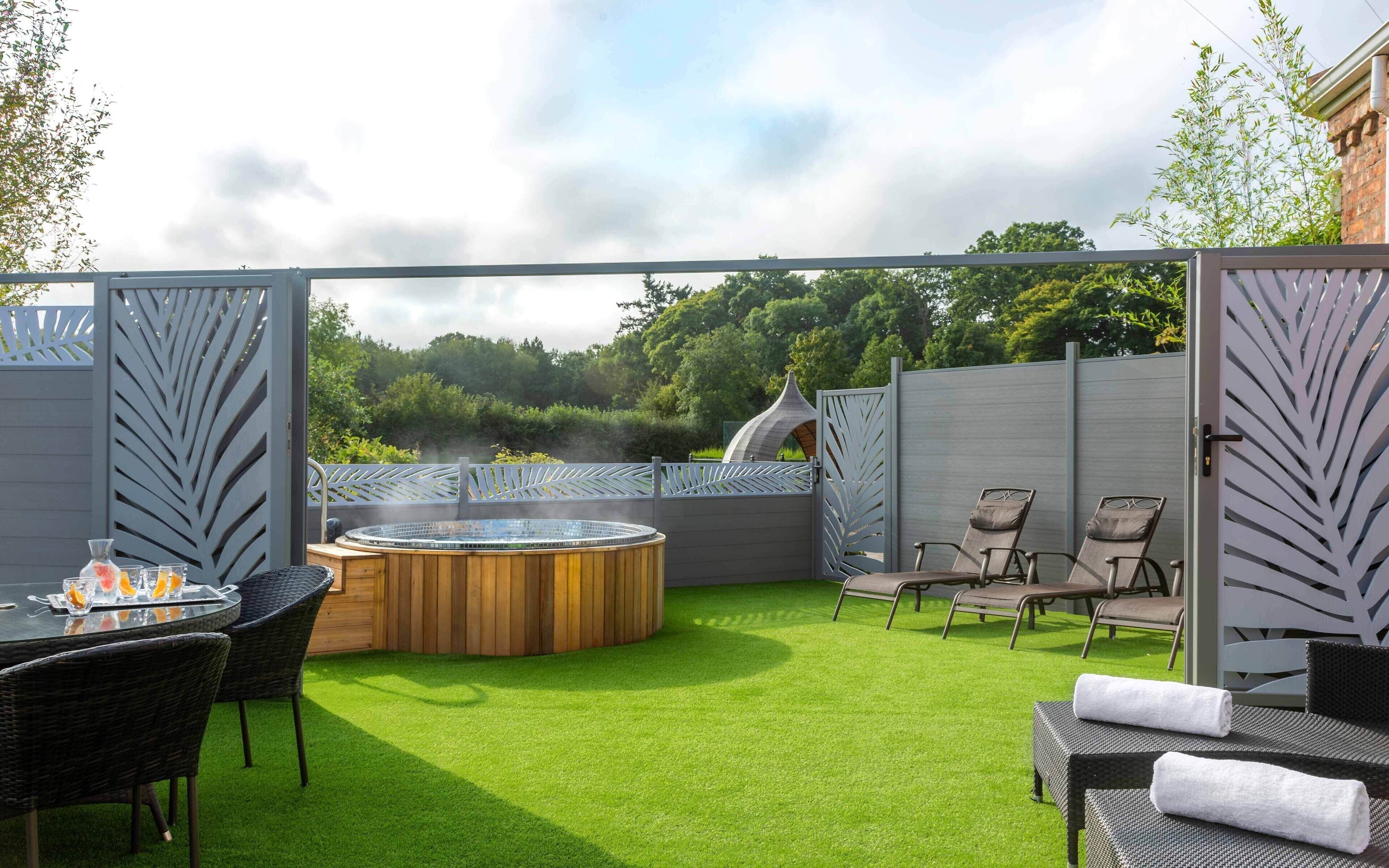 A patio area with a hot tub, outdoor seating, and a view of the surrounding greenery.