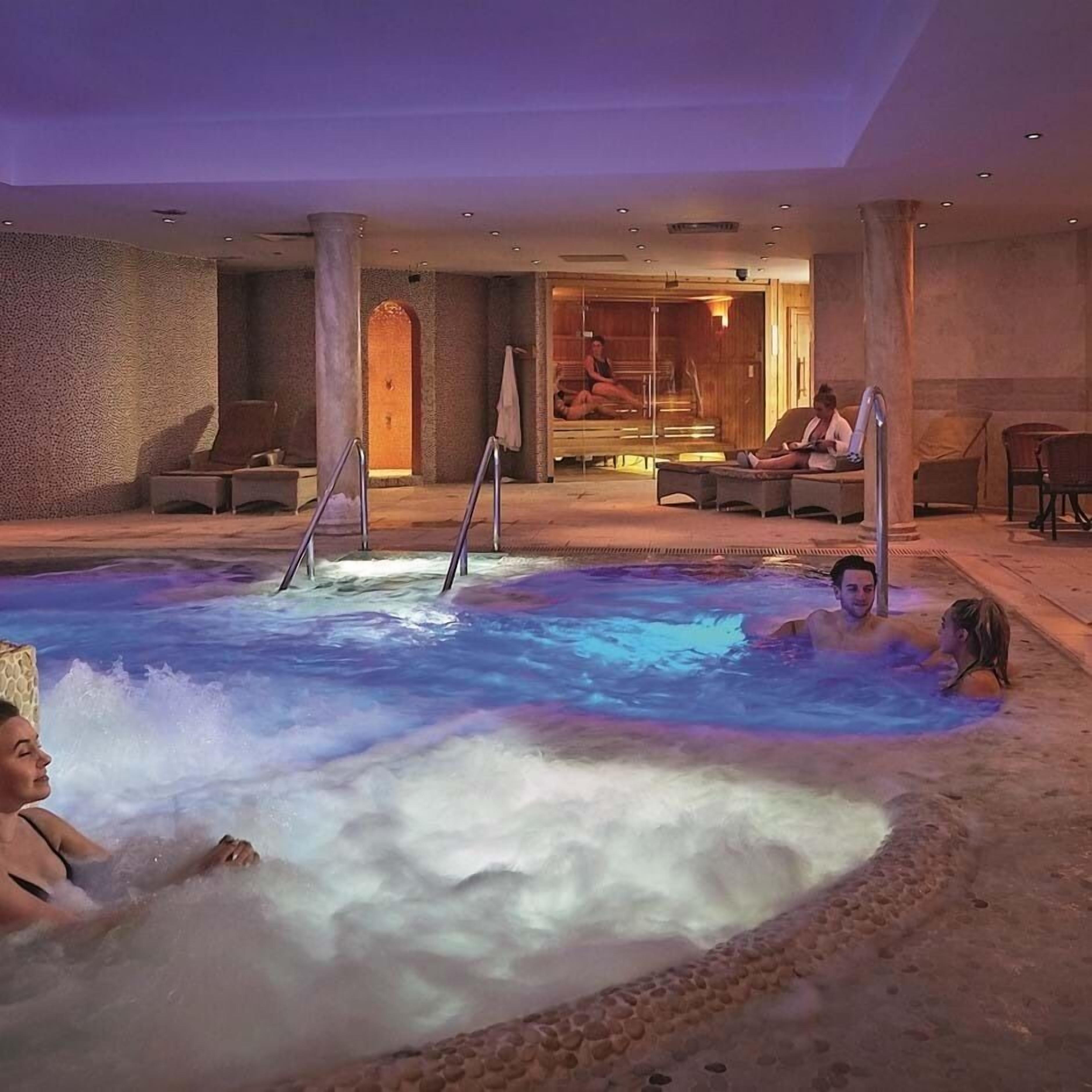 Un espace avec un jacuzzi où des personnes se détendent, un banc en bois et une porte vitrée donnant sur une pièce.