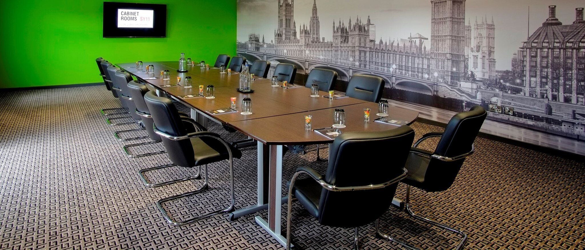 Une salle de conférence avec une longue table, des chaises noires et un mur vert.