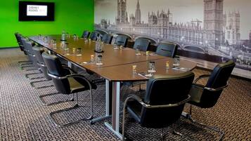 Une salle de conférence avec une longue table, des chaises noires et un mur vert.