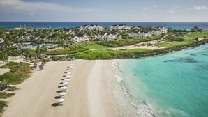 Luchtbeeld van een kustresort met strandvilla's, een zandstrand met parasols en een helder uitzicht op de oceaan.