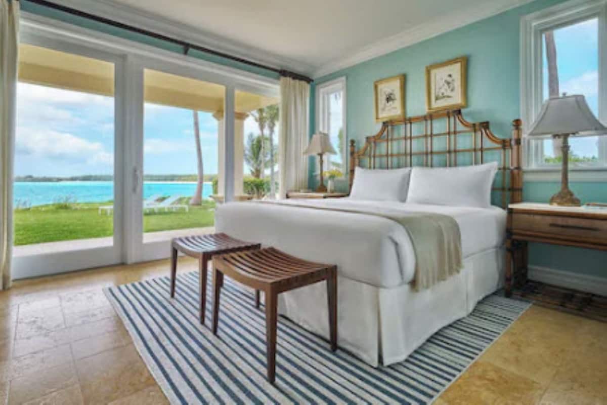 A bedroom with a large bed, a wooden headboard, a view of the ocean, a window, and a nightstand with a lamp.