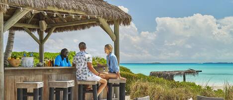 A wooden deck with a thatched roof, overlooking a turquoise sea.