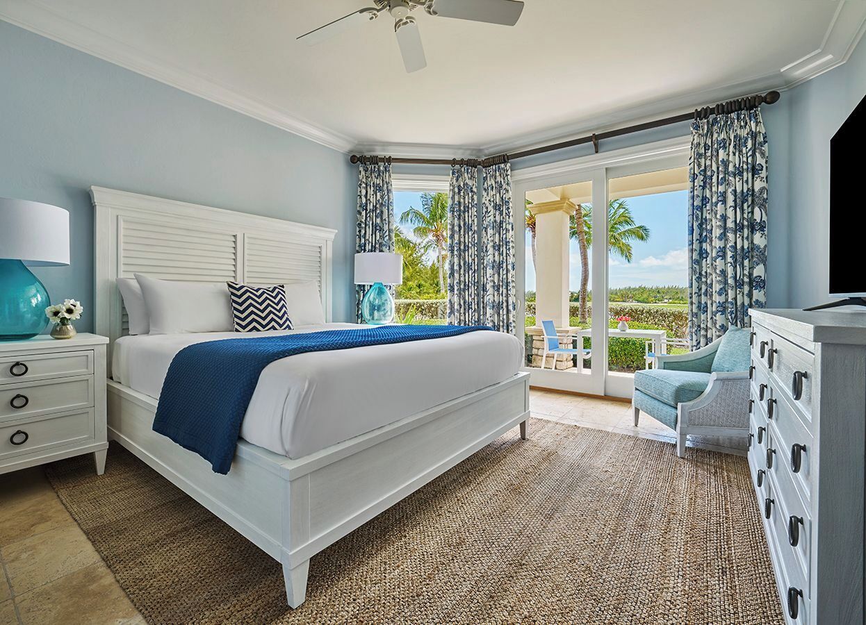 Quarto com cama, mesas de cabeceira, cômoda e vista para o exterior.