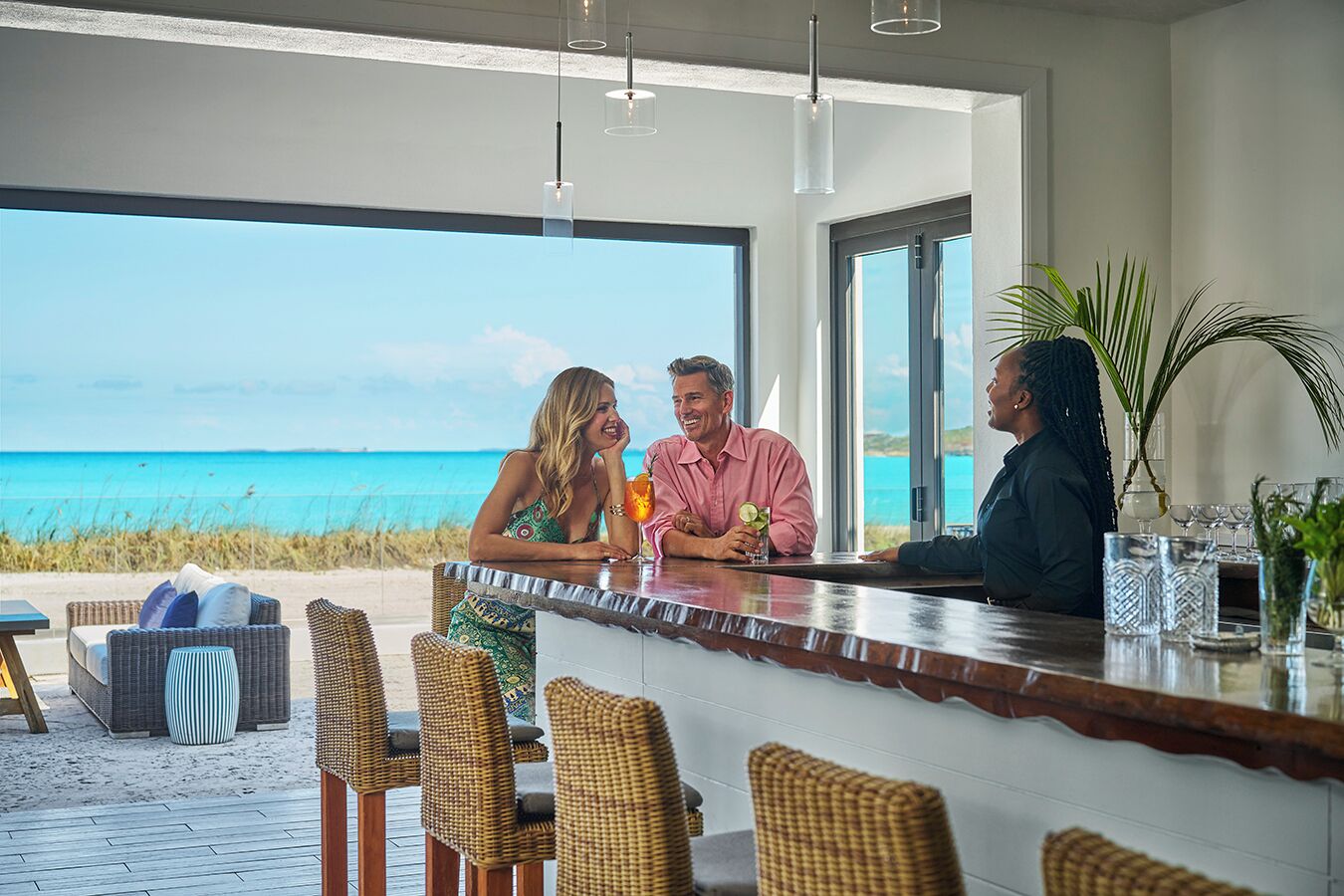 A modern bar area with wicker chairs, a large window overlooking the ocean, and a clear view of the beach.