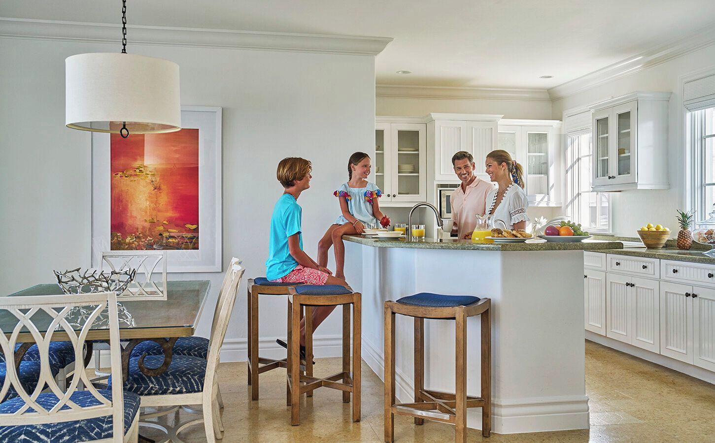 A modern kitchen with white cabinetry, a central island, and a dining area with a glass table and chairs.
