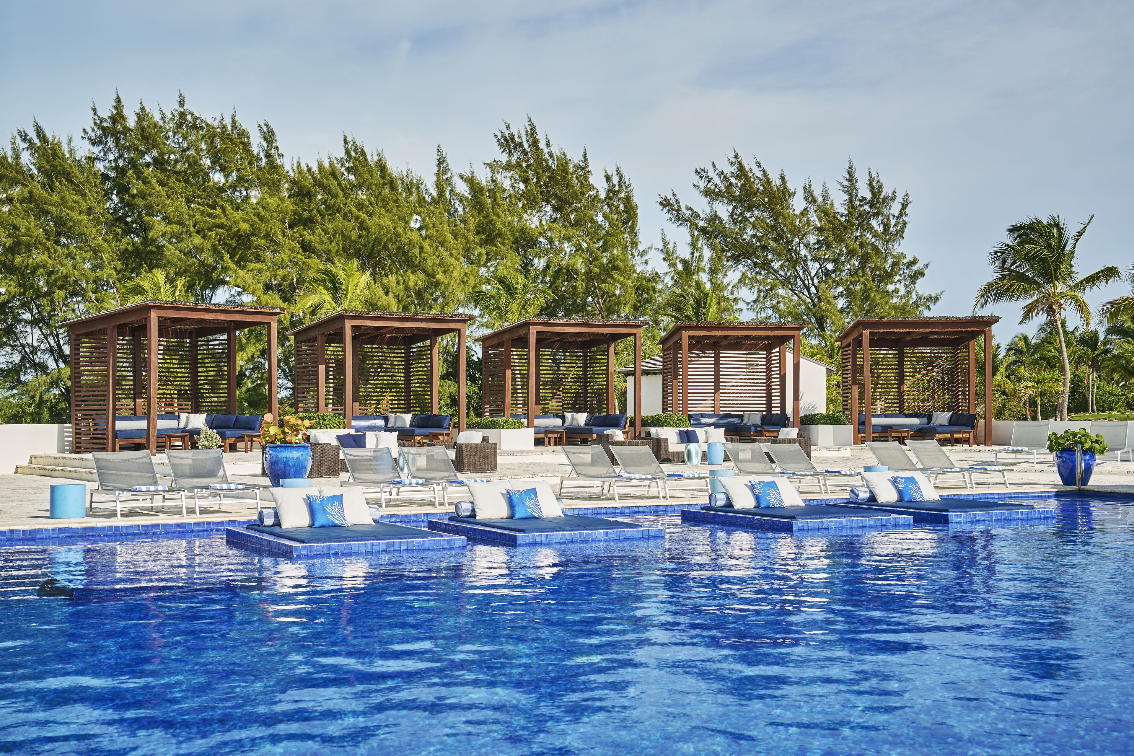 A pool area with lounge chairs and wooden gazebos, surrounded by palm trees.