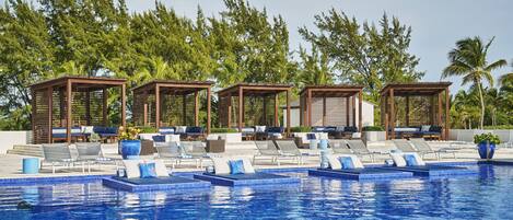A pool area with lounge chairs and wooden gazebos, surrounded by palm trees.