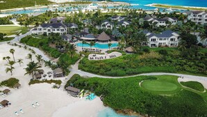 Luchtbeeld van een resort met meerdere gebouwen, een groot zwembad en een strand voorzien van ligbedden.