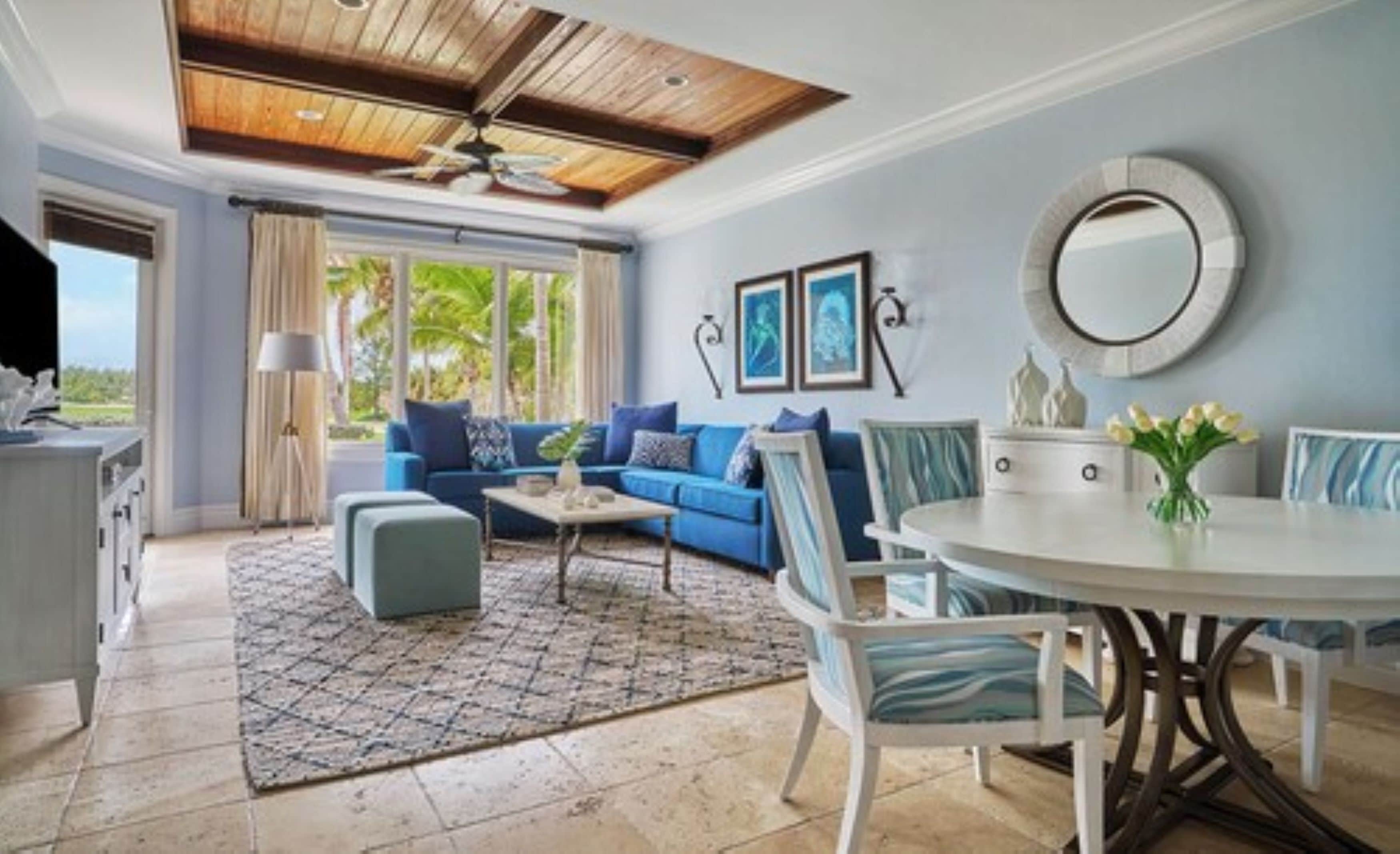 A living room with a blue sofa, a round dining table, and a ceiling fan.