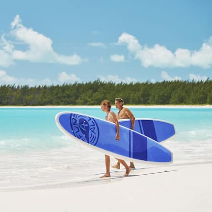 A beach scene with two people carrying a blue surfboard.