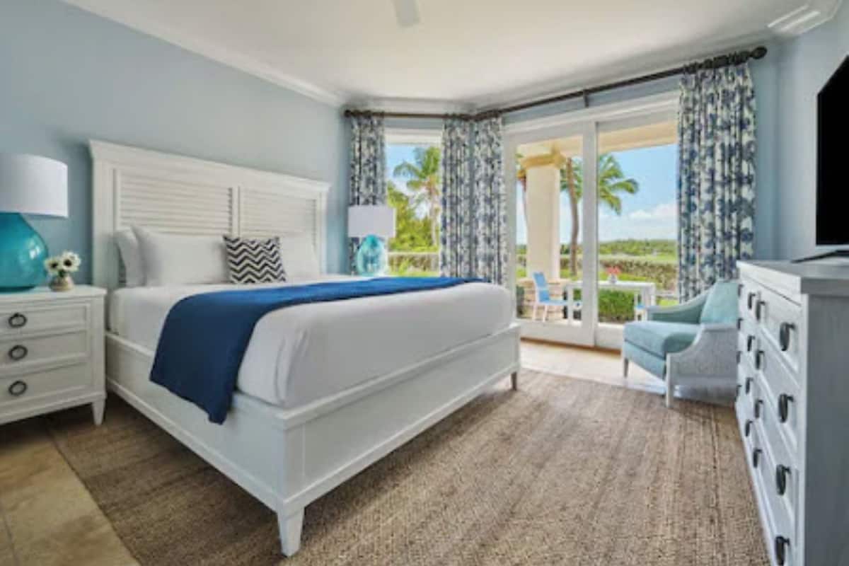 A bedroom with a large bed, a nightstand, a dresser, and a view of the outdoors.
