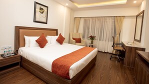 A hotel room with a large bed, a desk, a chair, a mirror, and a small table with a vase of flowers. - Southernstar Bangalore (Bengaluru)